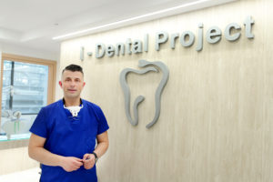 Ο Δρ. Καρατάσος Αλέξανδρος Χειρουργός Οδοντίατρος MSc, Dds δίπλα από το λογότυπο της κλινικής του στον Χολαργό